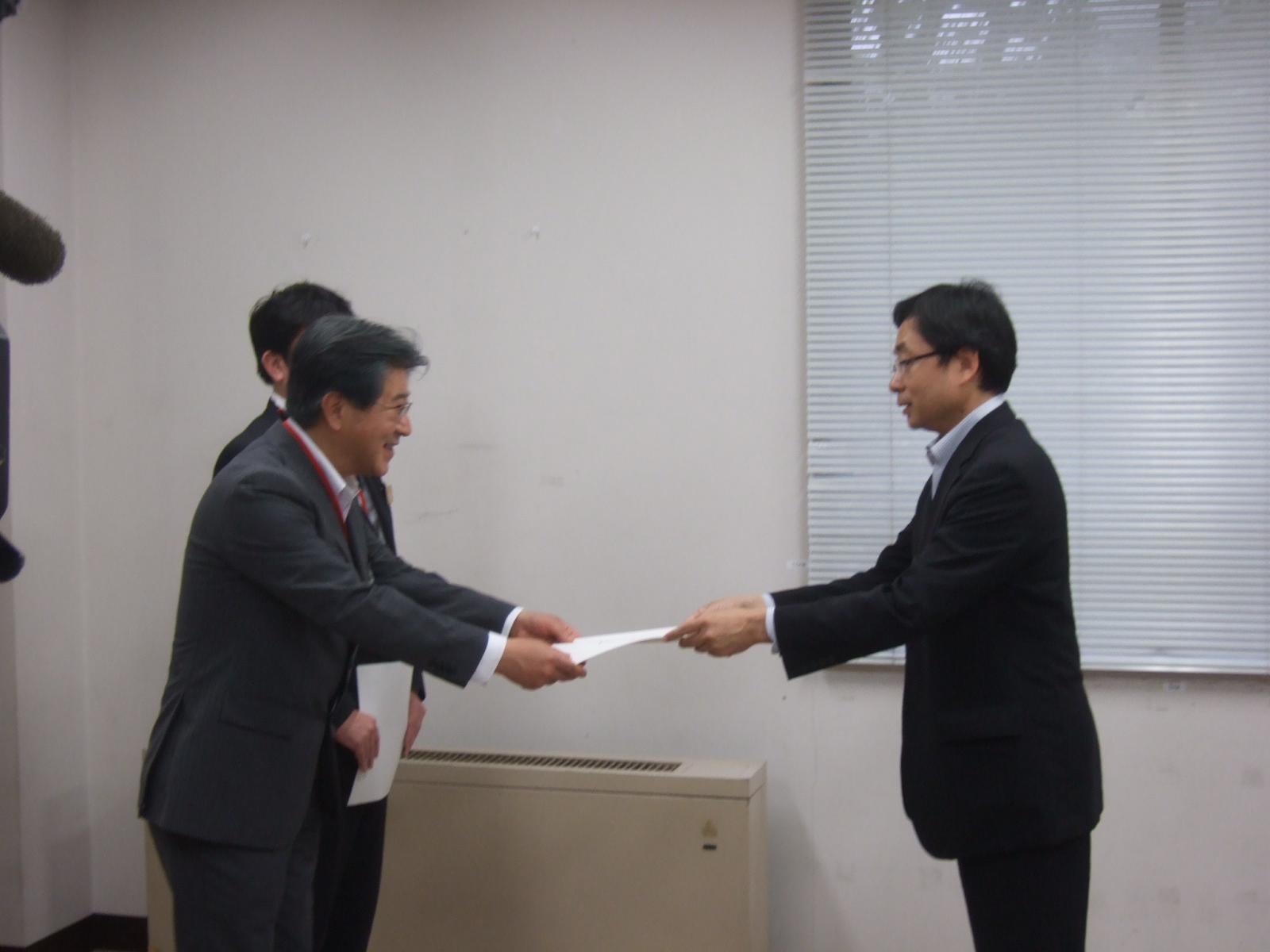 小沢市長が左側の男性と向かい合って立ち笑顔で連結許可書の交付を受けている様子の写真