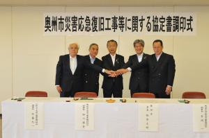 奥州市水道工事業協同組合、江刺上下水道工事業協同組合及び奥州金ヶ崎広域水道工事業協同組合の代表者と市長の5名が握手をしている写真