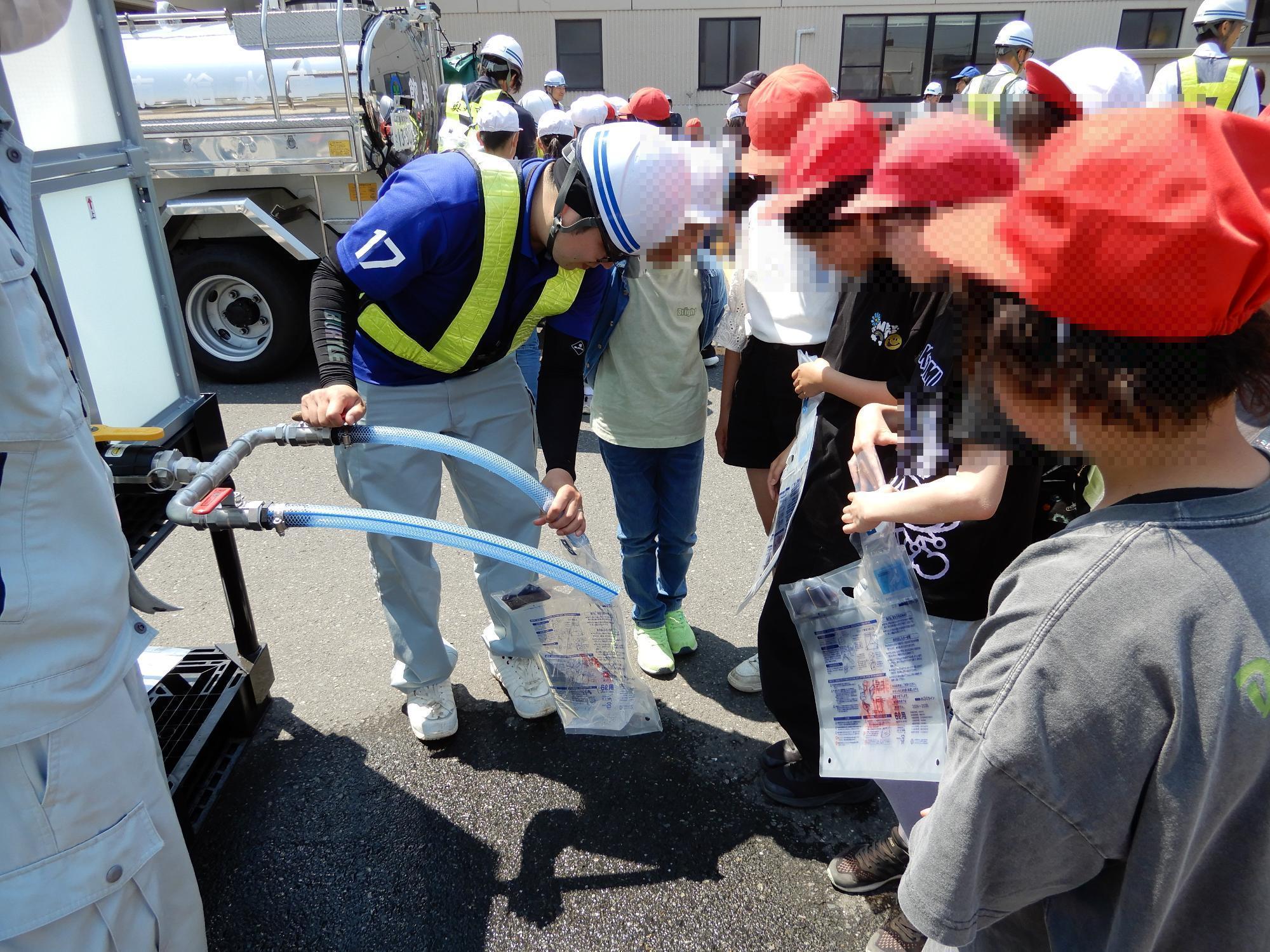 参加者が給水タンクに接続された蛇口を使用し給水袋へ水を汲んでいる様子の写真