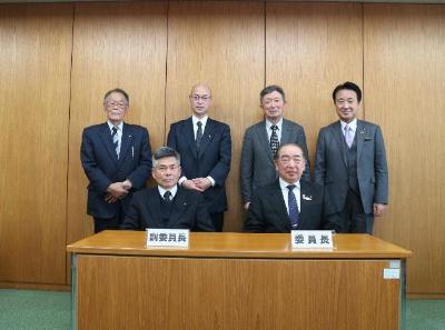 委員長と副委員長が席につき、その後ろに4名の委員が立っている総務常任委員会の方々の集合写真