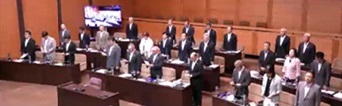 議場で席の前に立つ議員の方々を撮影した写真（奥州市議会 議会中継へのリンク）