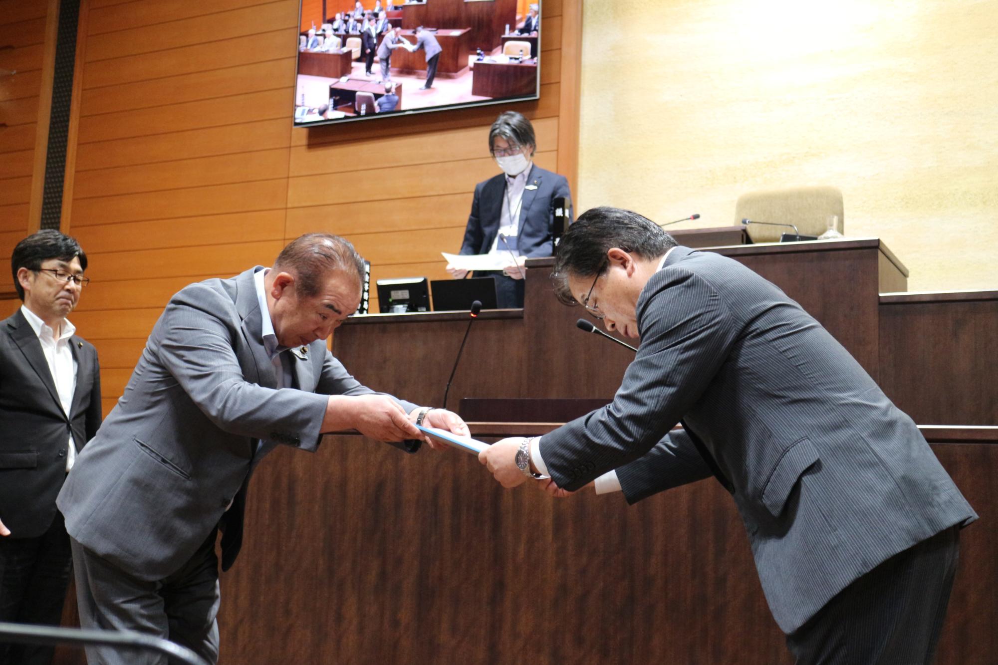 高橋浩総務常任委員会委員長が市長へ政策提言決議文書を手渡す様子