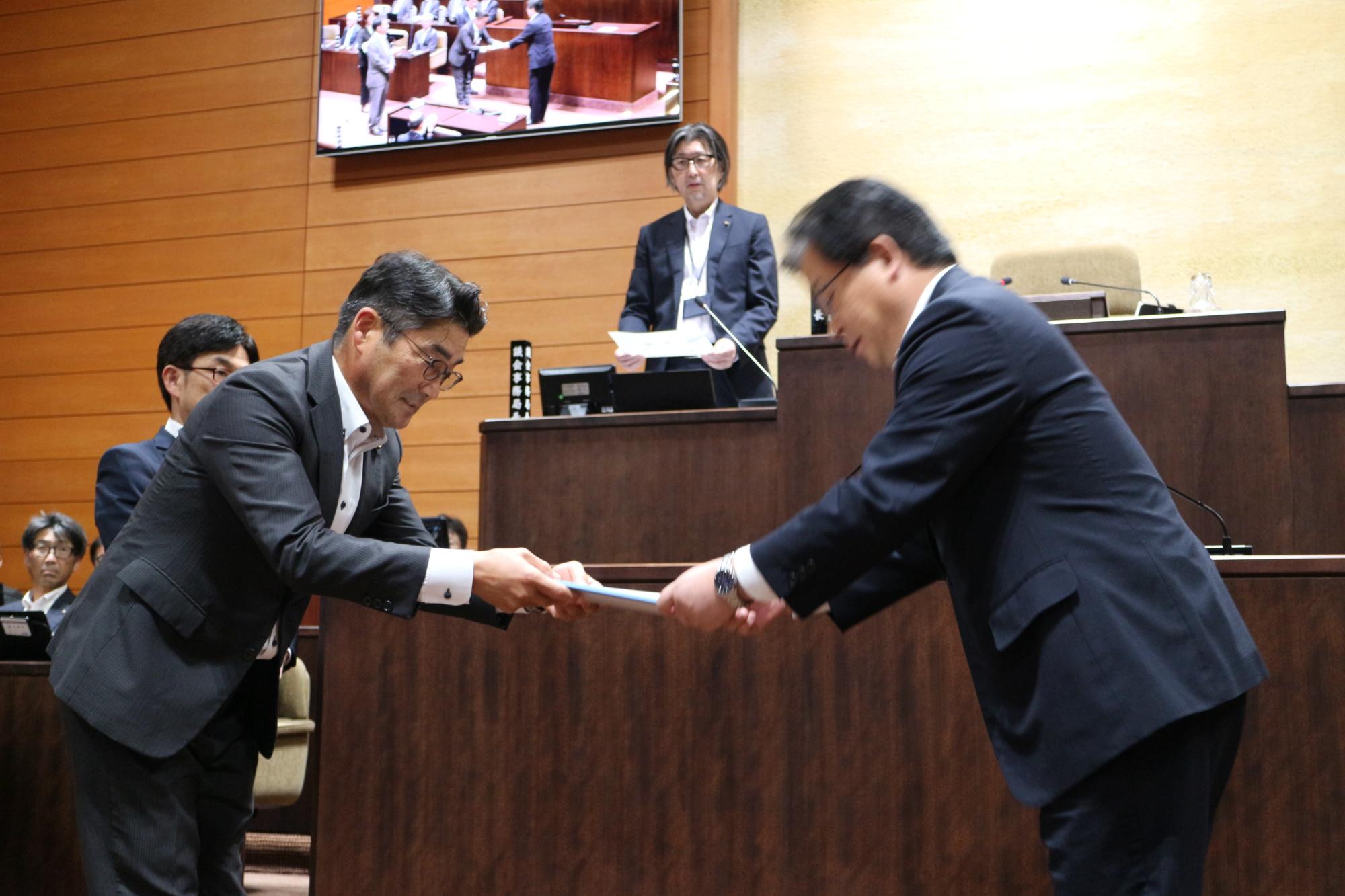 千葉和彦産業経済常任委員会委員長が市長へ政策提言決議文書を手渡す様子