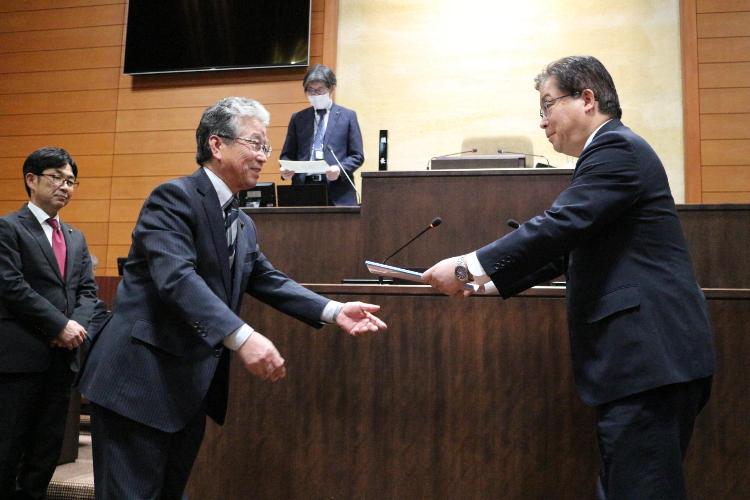 廣野富男建設環境常任委員会委員長が市長へ政策提言決議文書を手渡す様子