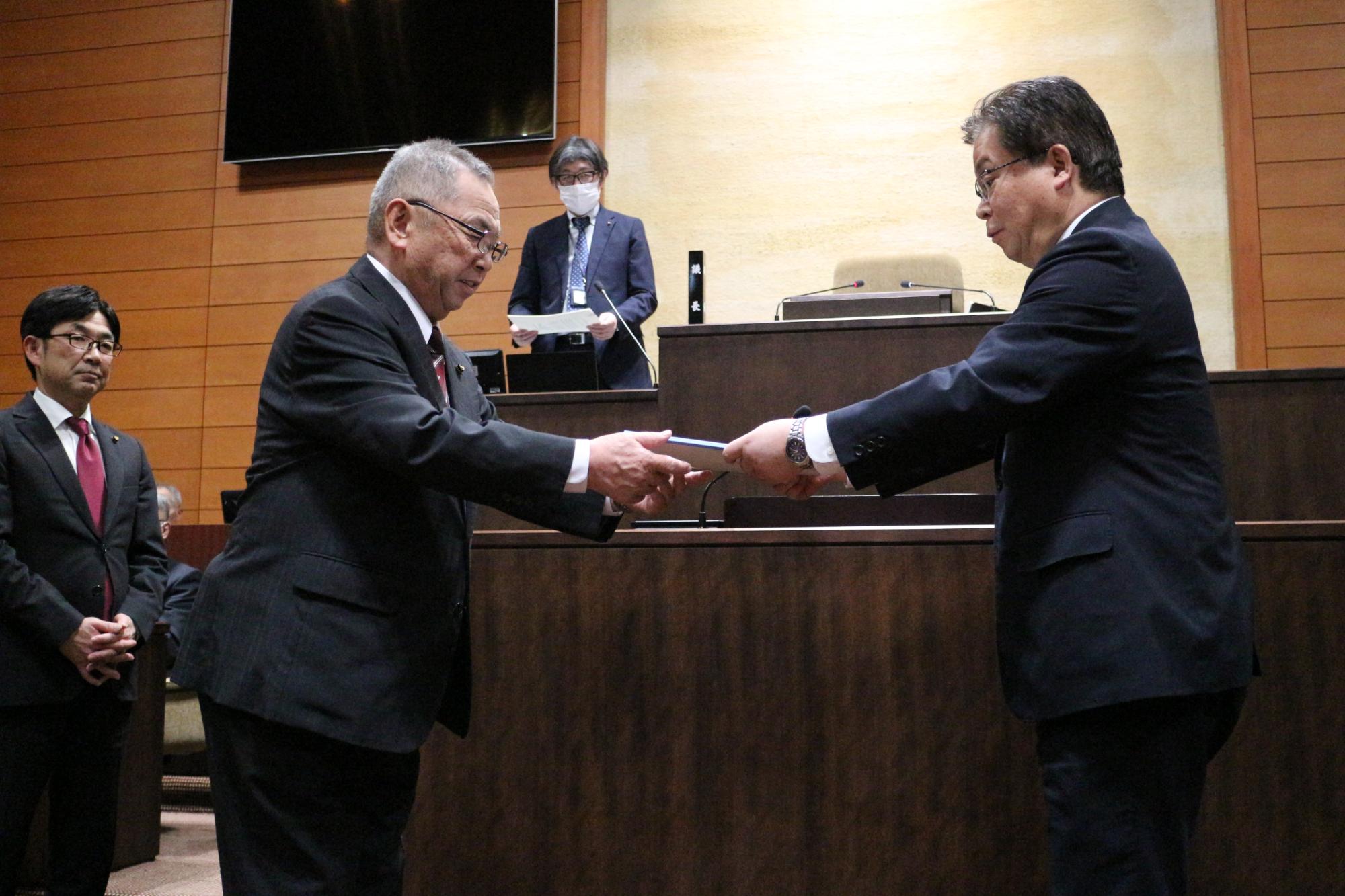 小野寺満教育厚生常任委員会委員長が市長へ政策提言決議文書を手渡す様子