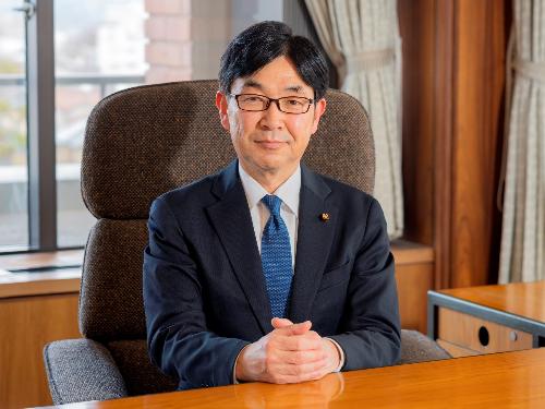 議長室の椅子に座っているスーツ姿で眼鏡をかけた菅原 由和議長を正面から撮影した写真