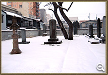 雪が降り積もった大安寺境内の墓所で、石灯篭といくつかの墓石が並んでいる写真