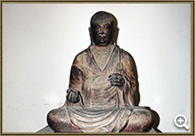 左手は掌を内に向け、右手は膝上で掌を仰ぎ、持ち物を持つ形で坐っている木造僧形坐像の写真