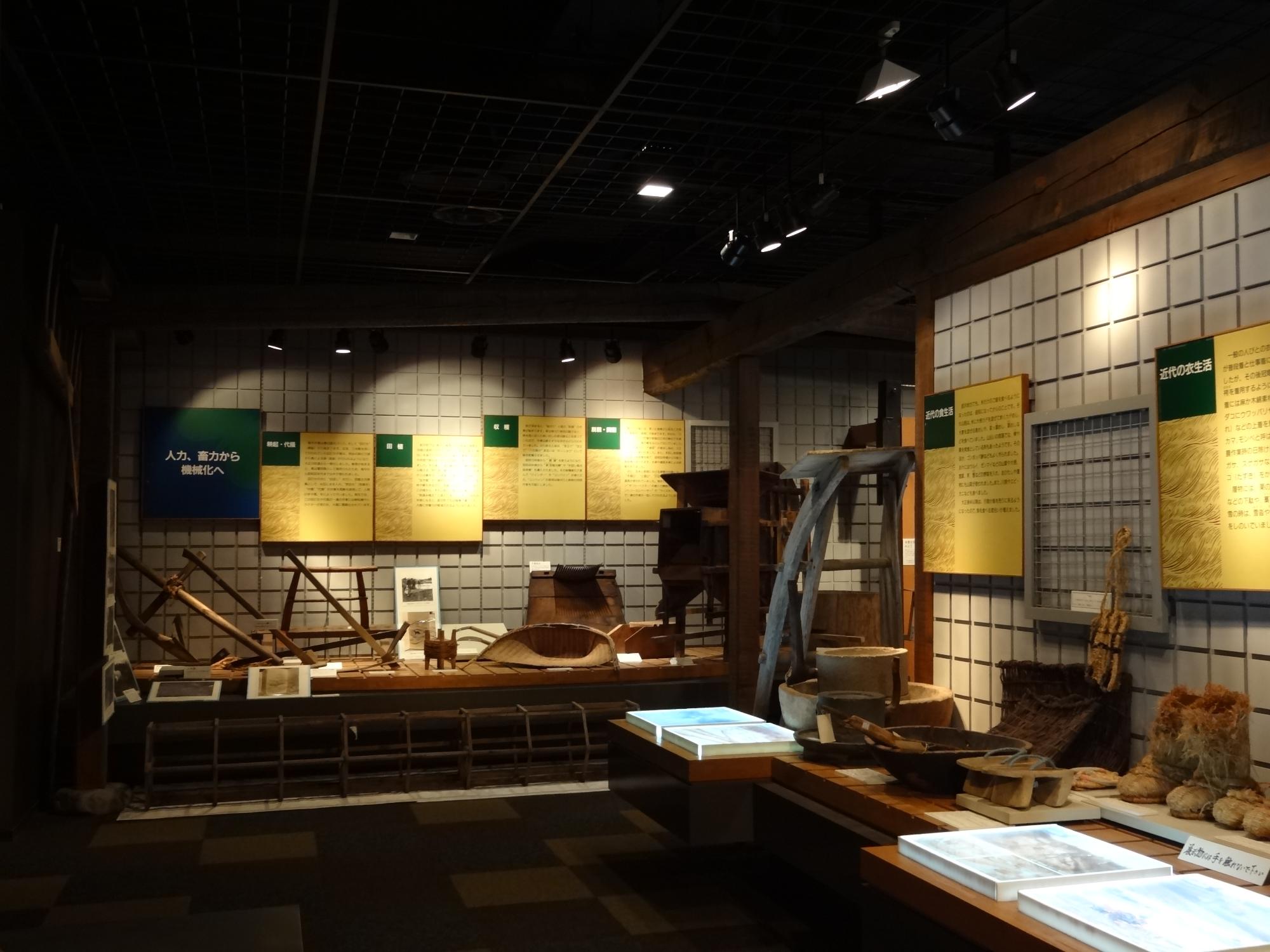壁に胆沢地域の歴史や民俗などを紹介するパネルが展示され、台の上に農具や民具、雪下駄などが並べて展示されている胆沢郷土資料館内部の写真