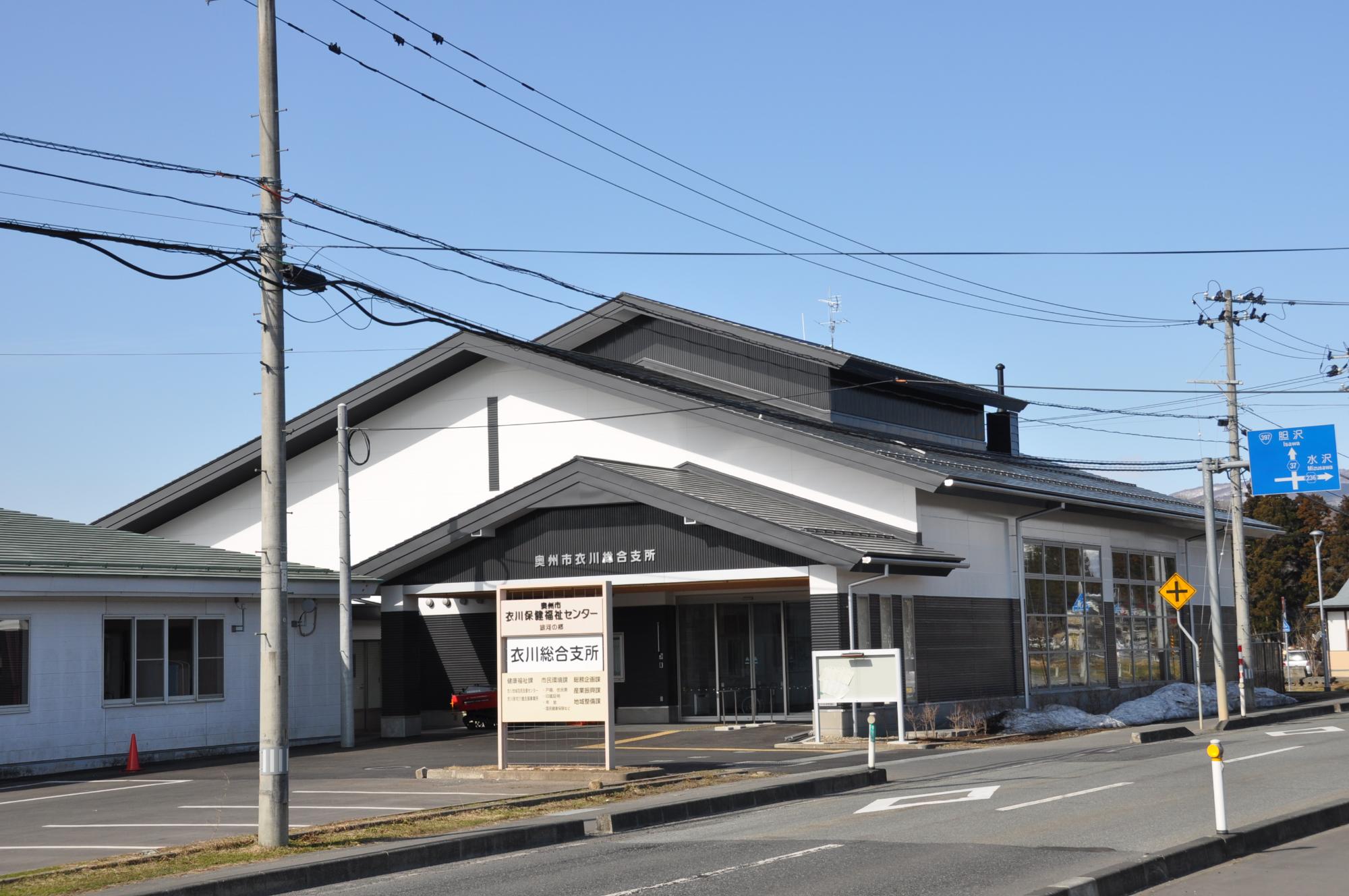 建物前の道路側に「衣川総合支所」と書かれた看板が立っており、黒い三角屋根、上部が白で下半分が黒色の外壁をした衣川総合支所の外観写真