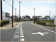 左側に歩道があり、十字路の先が右カーブになっている道路を写した写真