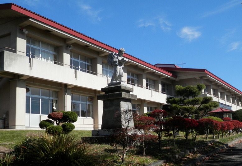 2階建ての校舎前に多くの植木や二宮金次郎の銅像が建てられている奥州市立稲瀬小学校の外観写真